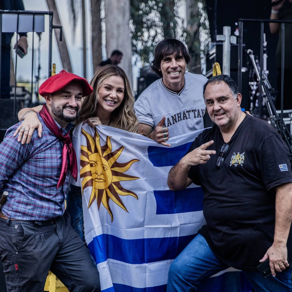 Claus e Vanessa posam com convidados e a bandeira do Uruguai ao lado do palco